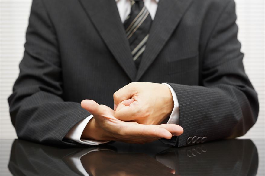 A person in a suit holding his hand up
Description automatically generated